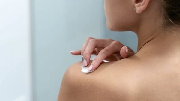 Mulher aplicando creme corporal no ombro no banheiro — Fotografia de Stock