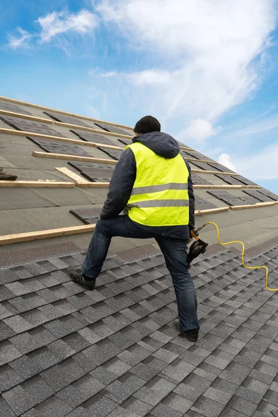 Trabajador usando pistola neumática de clavos instalar baldosas en el techo de la nueva casa en construcción —  Fotos de Stock