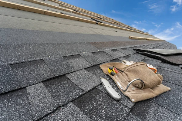 Asphalt tile roof and tool belt lying on new house under construction — Stock Photo, Image