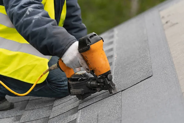 Trabajador usando pistola neumática de clavos instalar baldosas en el techo de la nueva casa en construcción —  Fotos de Stock