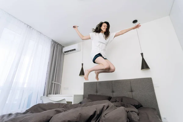 Fiatal felnőtt nő felébred, és ugrás az ágyon smartphone — Stock Fotó