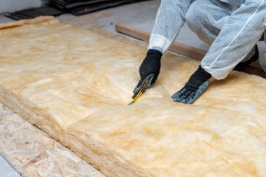 Profesyonel işçi termal yalıtım tabakasını çatının altına fiberglas yünü yerleştiriyor.