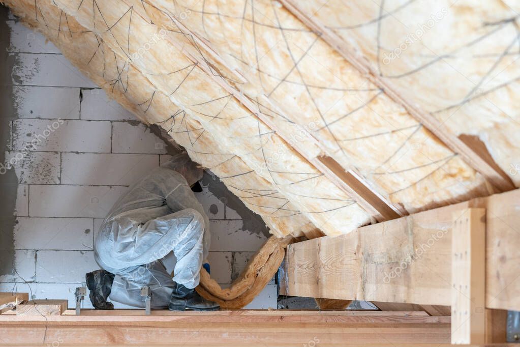 Professional workman installing thermal insulation layer under the roof