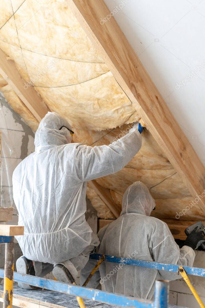 Two professional builder man installing thermal insulation rock wool under the roof