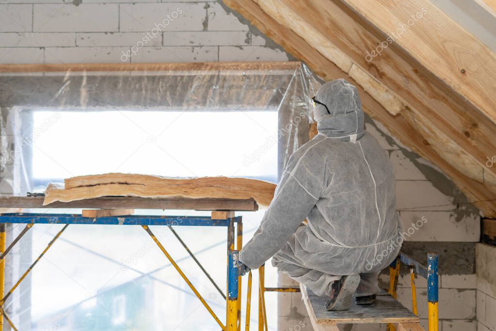 Professional roofer man installing thermal insulation layer with fiberglass wool under the roof
