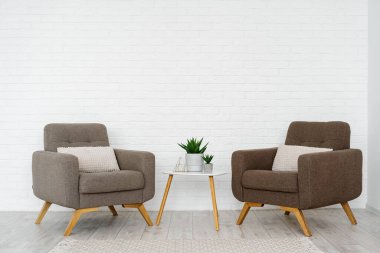 Modern oda İskandinav iç mimarisi, yastıklı mobilya, rahat koltuk, halı, ahşap üçgen sehpa ve çiçek saksısında beyaz tuğla duvarlı ev bitkisi.