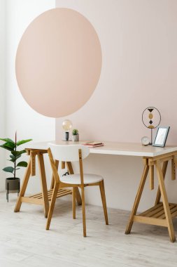 Ahşap masa, dekor, minimalist sandalye, yerde ev bitkisi ve duvarda fotokopi alanı olan geometrik resim ile modern iç mekanın dikey fotoğrafı