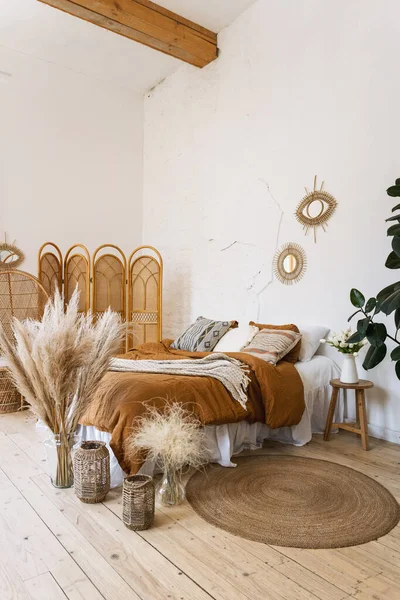 枕とベッドの上で再生されたブーブースタイルのインテリアで快適なベッドルームの垂直写真 ウィッカーバスケットの家の装飾 竹のドレッシング画面 花瓶の乾燥植物 — ストック写真