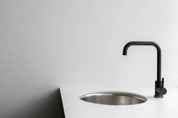 Sink and water tap against white copy space wall. Element of new kitchen with modern interior design at home