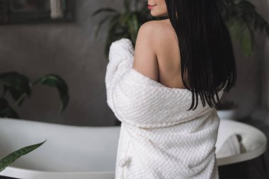 Çıplak omuzlu genç bir kızın beyaz banyoda bornozla dikilip sabah rutininden sonra...