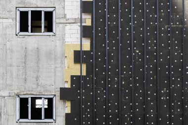 Konut geliştirme projesi kavramı. İnşaat halindeki binanın dış tarafında mineral kaya yünü, dış kısmında da beton duvar camları var.