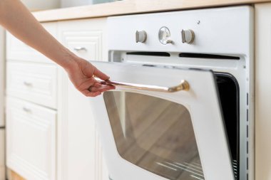 Fırın teçhizatı, pişirme ve yemek pişirme malzemelerinin üzerine yapılmış kadın eli açık görüntüsü. Beyaz iç mekanı olan modern bir mutfak.