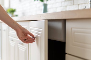 Mutfak dolabındaki mobilyaların üzerinde el açık duran, beyaz iç tasarımla modern bir evde duran kadın manzarası.