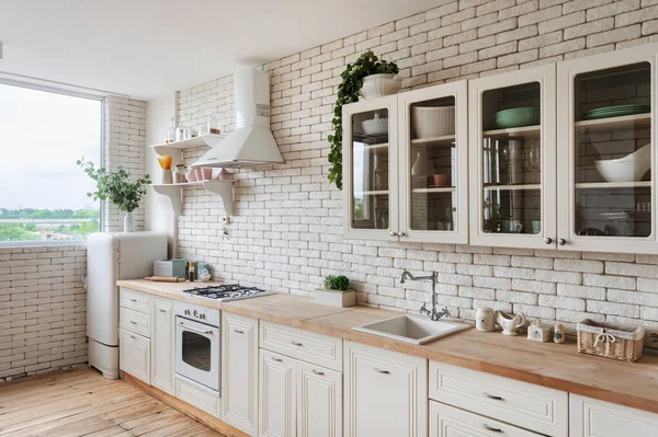 Cooking hood over gas stove appliance, built in oven equipment, sink and water tap, kitchenware supplies on shelves, green plants on cupboard furniture. Side view of white kitchen facade in apartment