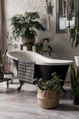 Modern banyo dikey fotoğrafı zarif küvet, tekstil havlusu, beyaz duvarda ayna ve çiçek sepetinde yeşil bitkiler.