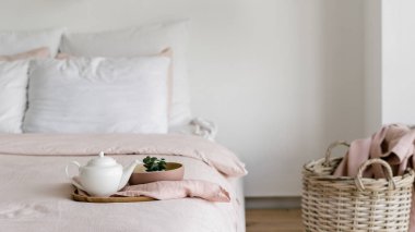 Evde sabah hafta sonu kavramı. Parlak yatak odası, yorgan, yastık ve çaydanlık ile panoramik manzara rahat yatakta çamaşır sepetine karşı