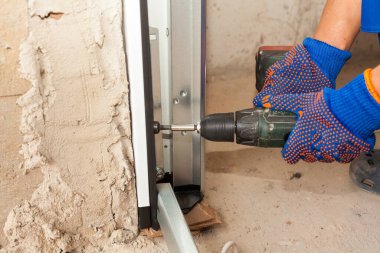 Geliştirme konsepti. Profesyonel işçinin kırpılmış görüntüsü, inşaat halindeki yeni evdeki garaj kapısı sistemine fotokopi duvarının yanındaki elektrikli tornavida kullanarak metal demiryolu döşemesi