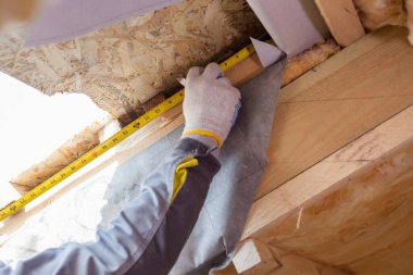 İnşaat halindeki ev kavramı. Profesyonel bir işçinin kapalı alanda bitmemiş bir binada durup mezura kullanması, tavandaki ahşap tahtanın uzunluğunu kontrol etmesi.