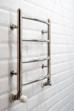 Modern apartmandaki beyaz banyonun dikey fotoğrafı. Yeni ısıtılmış havlu tırabzanı fotokopi alanı arka planında fayanslı duvara dayalı.