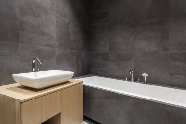 Çağdaş iç tasarımı olan yeni ve modern ev unsuru. Beyaz küvetli banyo ve ahşap tezgahın üzerindeki lavabo gri fotokopi duvarına karşı.