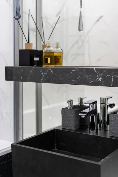 現代的なインテリアデザインの現代的なバスルームでミラーの近くの棚の上に新しい黒いシンク 石鹸ディスペンサーと香りスティック上の銀蛇口の垂直側のビュー — ストック写真