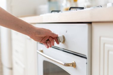 Kadın el açma düğmesinin fırın teçhizatında açık olması kontrol panelinde sıcaklığı değiştirmesi, mutfakta durması. Beyaz iç tasarımı olan modern bir ev.