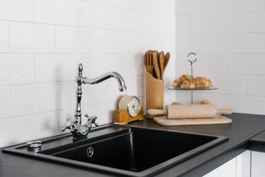 Lavaboyu ve gümüş musluğu kapayın. Siyah tezgahın üzerinde, fayanslı duvara karşı. Çağdaş mutfak odası olan modern evde yemek ve kruvasan yiyecekler.