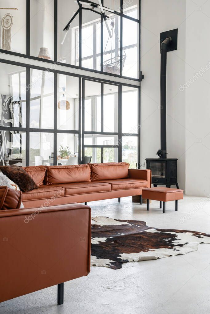 Vertical photo of modern living room with contemporary interior design, fireplace near leather couch on concrete floor with skin carpet, against glass wall on background