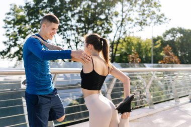 Takım çalışması aktivite konsepti. Mutlu genç arkadaşlar birbirlerine destek oluyor, spor eğitimi alıyorlar, birlikte koşmadan önce bacaklarını esnetiyorlar.