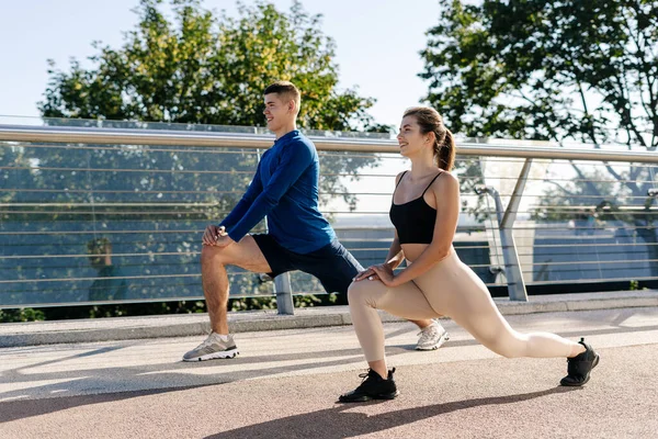 健康和积极的生活方式的概念 快乐的成年男女一起参加户外运动训练 做健美运动 跑步前伸展下半身 开怀大笑的侧观 — 图库照片