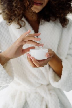 Güzellik prosedürü kavramı. Ellerinde krem tutan, bornozla ayakta duran ve sabahları banyoda geçiren Afro-Amerikan kadının dikey görüntüsü.