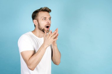 Vay canına, inanılmaz. Şok olmuş, şaşırmış, yana bakan, beyaz tişörtlü mavi fotokopi arkaplanda tek başına duran genç adamın yan görüntüsü. İnanılmaz ve beklenmedik haberler kavramı