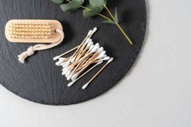 Ekolojik ve geri dönüşümlü nesneler kavramı. Düz uzanma, banyo malzemelerinin üst görüntüsü, tırnak fırçası, ahşap kulak çubukları ve okaliptüs bitkisi siyah plaka standı üzerinde beyaz fotokopi alanı arka planına karşı.