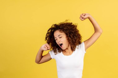 Uyuyan genç Afro-Amerikan kadın portresi esniyor, uzanıyor ve ellerini kaldırıyor, pazartesi sabahı erken saatlerde uyanıyor ve sarı fotokopi alanı arka planında duruyor.