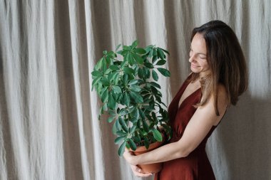 Gri perde arkasında duran ve geniş bir gülümsemeyle gülümseyen çiçekli mutlu genç kadının yan görüntüsü. Bitki bakımı ve bahçıvanlık hobisi