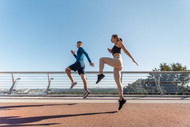 Sağlıklı yaşam tarzı kavramı. Genç yetişkin bir kadın ve aktif bir adamın açık havada spor yaparken, şehirde yüksekten atlarken alçak açılı ve yandan görünüşü.