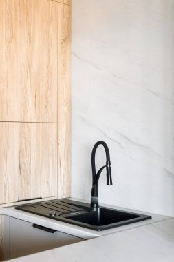 Bu mutfak, modern bir muslukla modern iç tasarımın ahşap ve mermer elementleriyle kusursuz bir şekilde harmanlanmış parlak siyah bir lavabo içeriyor ve evde işlevsel bir alan yaratıyor.