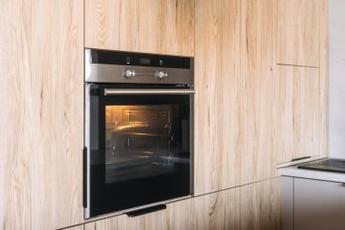 Ev aletleri. Modern mutfak, modern tasarım elementlerini ahşap dolaba kusursuzca entegre edilmiş siyah bir fırınla sergiliyor, şık ve verimli bir yemek alanı sunuyor..