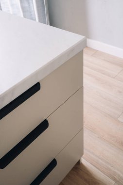 Mutfak tezgahının altında depolama malzemeleri için çekmeceler. Bu çağdaş oda, siyah aksanlı, temiz beyaz tezgahlı, yüksek açılı manzaralı minimalist dolaplara sahiptir.