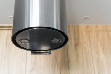 Tavandan sarkan şık bir mutfak kaputu, minimalist paslanmaz çelik tasarımı içeriyor. Ahşap zeminin arka planı oda alanının modern estetiğini geliştirir..