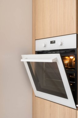 Modern bir mutfak vitrininde minimalist tasarımı olan parlak bir fırın var. Yemek pişirmek için ev aletleri. Sıcak ahşap paneller dolabın temiz çizgilerini tamamlıyor.