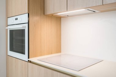 Yeni çağdaş mutfak vitrinlerinin yan görünüşü şık bir indüksiyon hobisi ve minimalist kabine entegre edilmiş dahili bir fırın. Sıcak ahşap tonlar uzayın modern atmosferini arttırır..