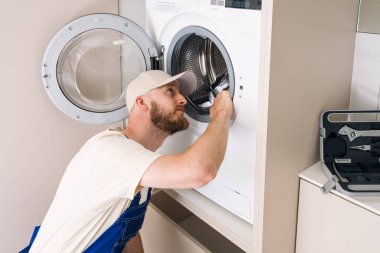 Çağdaş bir çamaşır odasında çamaşır makinesinin içini inceleyen bir adam. Mekanda modern aletler var. Evde ev aletleri, yıllık bakım.