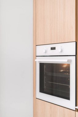 Modern mutfaktaki şık bir fırının dikey çekimi. Tasarım, minimalist elementleri ve hafif ahşap dolapları içeriyor.