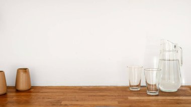 Mutfak tezgahında seramik sürahisi ve birkaç bardak bulunan minimalist dekor unsurlarıyla tamamlanmış bir su sürahisi var. Dairenin boho estetiğini artırıyor, arka planda beyaz fotokopi alanı var.