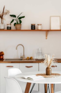 Yemek masasında açık bir kitap. Hafta sonları evde dinlenme kavramları. Yavaş yaşam estetiği. Beyaz bir tezgah ve doğal bir dekor tarafından vurgulanmış, temiz ve modern bir tasarım içerir.