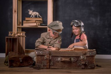 Pilotu oynayan çocuk ve kız. Eski moda çocukların gözlüklü portresi ellerinde pusula ve dürbünle eski bir bavula oturmuş. Yenilik, seyahat ve araştırma.