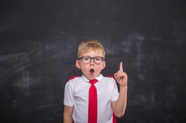 Mutlu gülümseyen okul çocuğu sol tarafı gösteriyor. Okul satışına geri dönüyoruz. Tahtaya karşı üniformalı çocuk.