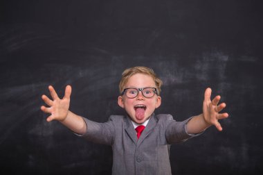 Üniformalı ve gözlüklü komik okul çocuğu kameraya doğru kollarını açıp dil gösteriyor. Karatahtaya karşı şaşkın suratlı mutlu çocuk. Okula dönelim. Eğitim başarısı yenilik konsepti
