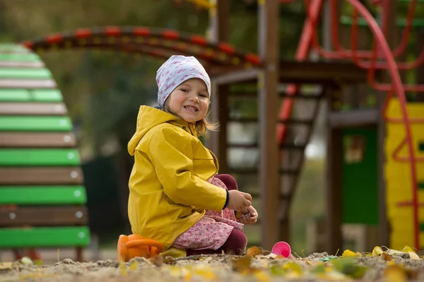 Happy child girl in yellow coat playing outdoors in playground. Sunny autumn day.